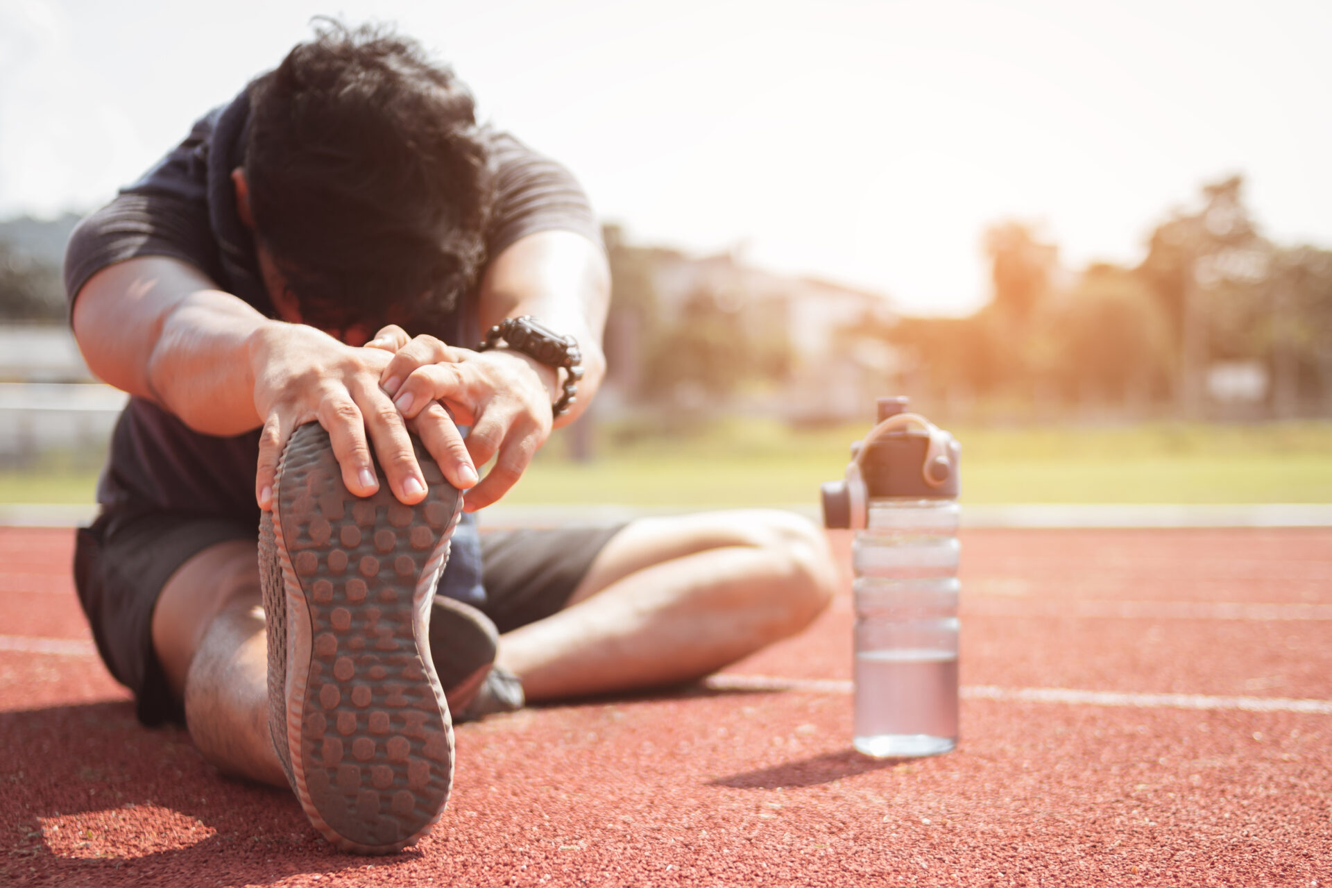 Un homme assis sur une piste d'athlétisme faisant des étirements d'ischio-jambiers et mollets