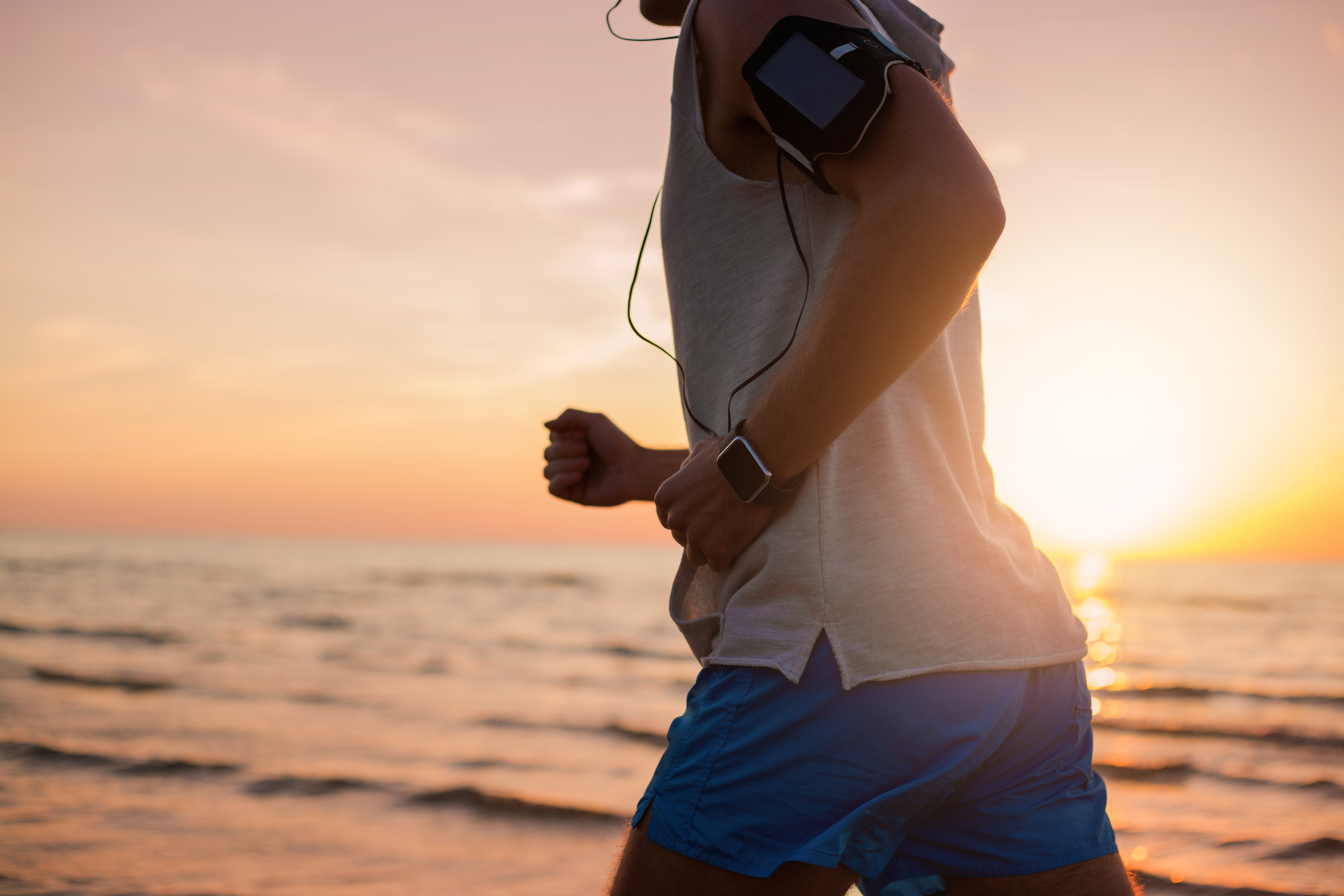 Un homme courant sur la plage avec une playlist dans les écouteurs